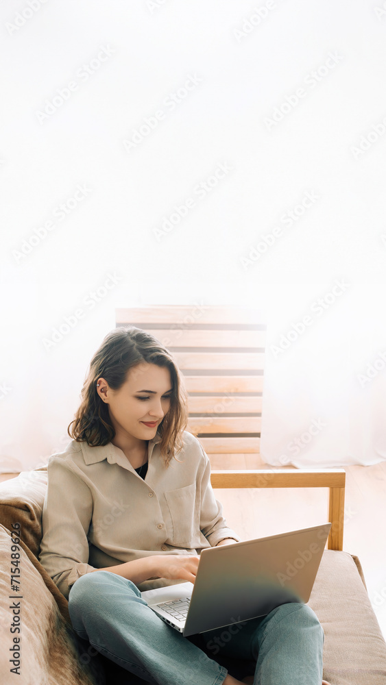 Cheerful millennial woman typing on a laptop, attending a virtual meeting while seated on a sofa with a gadget. Joyful millennial woman typing on a laptop attending a virtual meeting seated on a sofa. Cheerful millennial woman typing on a laptop, attending a virtual meeting while seated on a sofa with a gadget. Joyful millennial woman typing on a laptop attending a virtual meeting seated on a sofa.