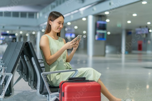 Asian woman with luggage using phone while waiting for departure at a transportation departure hall