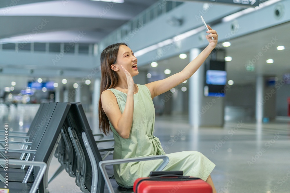 Asian woman with luggage using phone video call while waiting for departure at a transportation departure hall Asian woman with luggage using phone video call while waiting for departure at a transportation departure hall