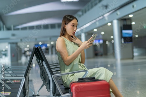 Asian woman with luggage using phone while waiting for departure at a transportation departure hall
