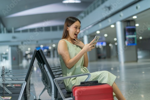 Asian woman with luggage using phone while waiting for departure at a transportation departure hall