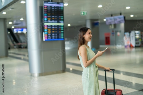 Asian woman with luggage using phone to check travel information at a departure terminal