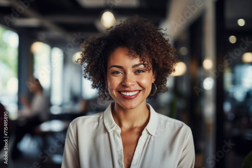 Smiling African American lady with curly hair and casual clothing standing in an office, radiating happiness and beauty