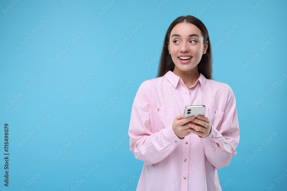 Happy woman sending message via smartphone on light blue background, space for text Happy woman sending message via smartphone on light blue background, space for text