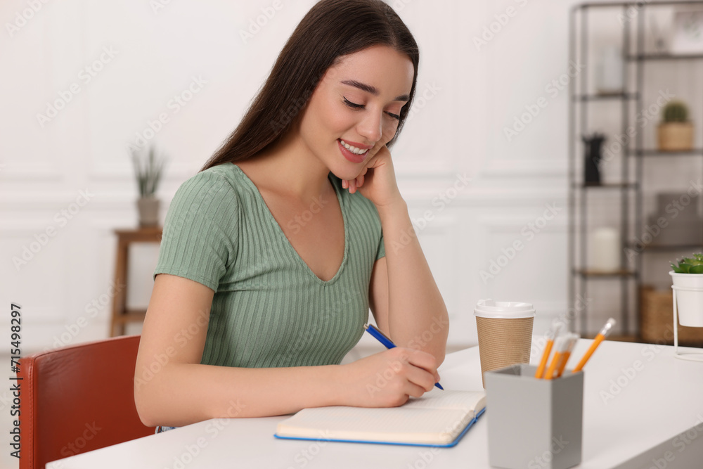 Young woman writing in notebook at white table indoors Young woman writing in notebook at white table indoors