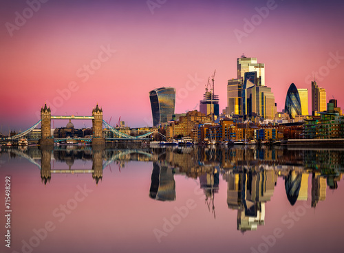 The skyline of the City of London and Tower Bridge during pink dawn and sunrise with relfections in the River Thames, England