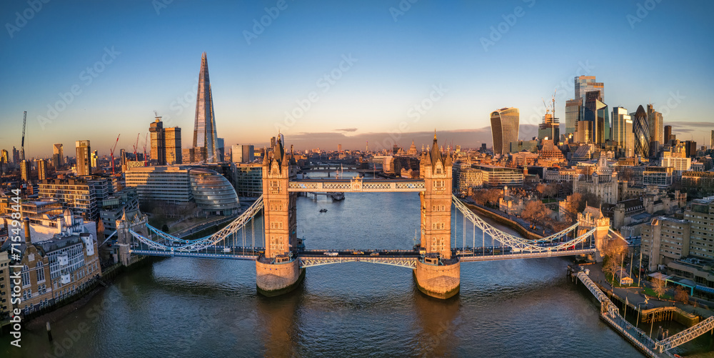 Aerial front view of the Tower Bridge of London with the skyline behind reflecting the golden sunrise light, England