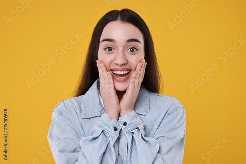 Portrait of happy surprised woman on yellow background