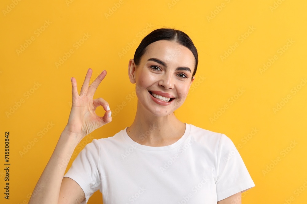Beautiful woman with clean teeth smiling and showing OK gesture on yellow background