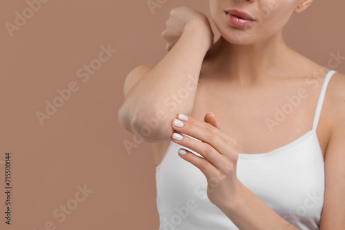 Woman with dry skin checking her elbow on beige background, closeup. Space for text