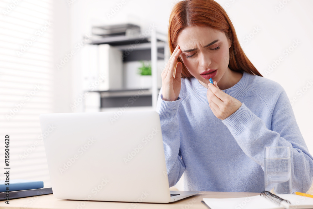 Woman with pill suffering from headache at workplace in office