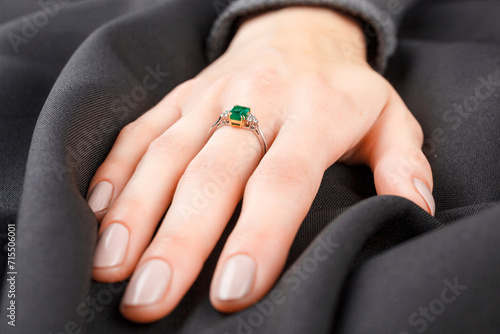 Beautiful female hand with gold ring with diamonds and emerald on gray background