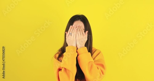 Woman covers hands with palms, hides face, plays hide and seek. Confused excited woman open face looking at camera with big eyes in surprise, shocked. Oh my god wow. Peekaboo isolated on yellow wall.