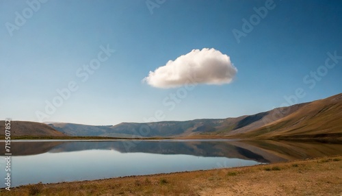 a lonely cloud over a mountain pick reflects on a lake in a dusty and soft landscape