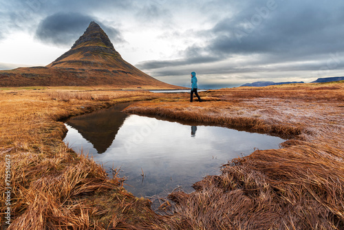 Woman walks in front of the famous Kirkjufell mountain reflecting in the water of a small lake, Snaefellsnes Peninsula, Western Iceland, Iceland, Polar Regions photo