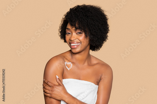 Happy woman with lotion heart on shoulder wrapped in towel
