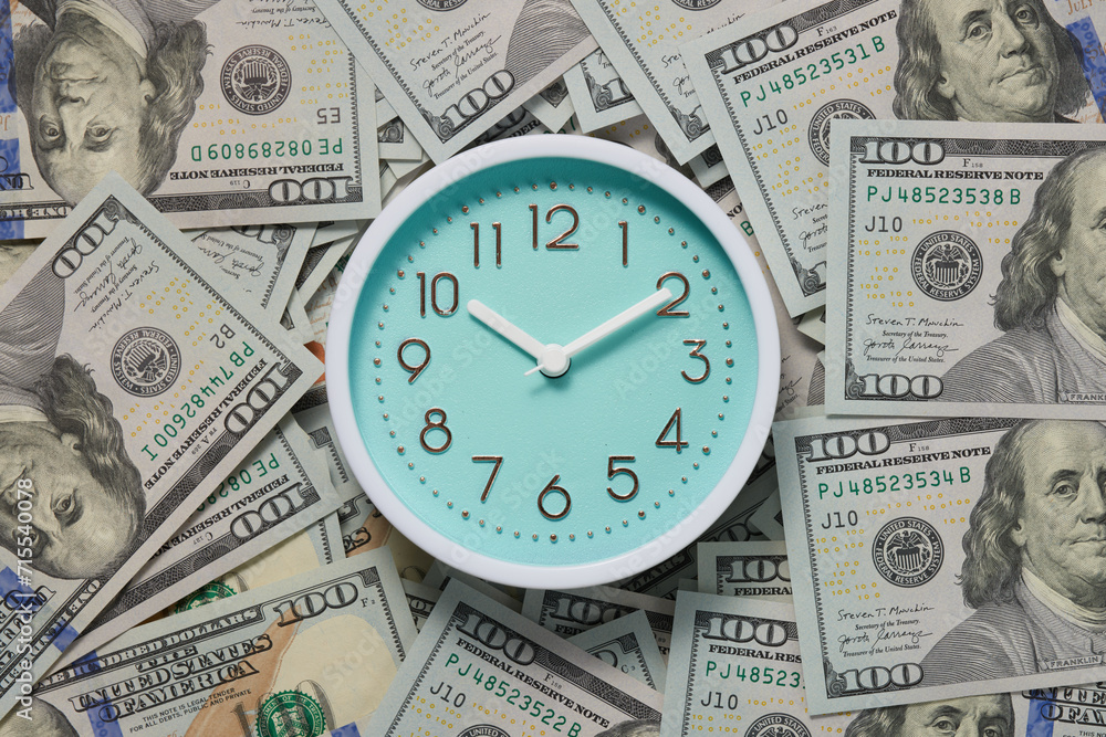 Round analog clock on many hundred dollar bills top view. Round analog clock on many hundred dollar bills top view.