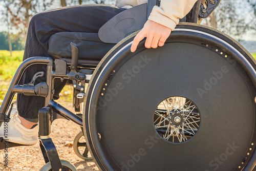 Close-up of cropped unrecognizable young woman's hand on the wheel of her wheelchair in the park photo