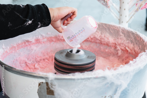 Close-up of a cropped unrecognizable hand pouring sugar into a cotton candy machine with pink candy floss forming inside photo