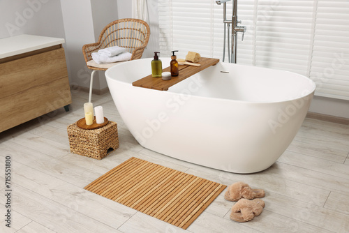 Stylish bathroom interior with bamboo bath mat and white tub photo