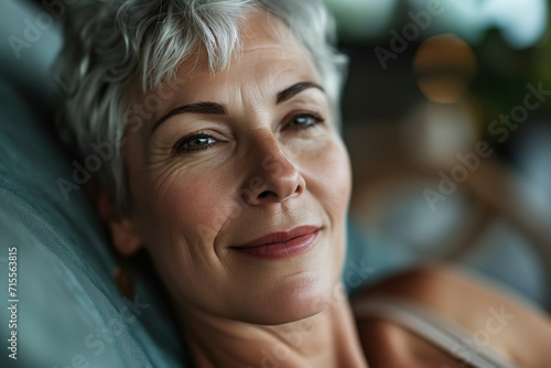 Close-up portrait of senior woman resting lying on pillow indoors and looking at camera