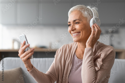 senior lady in headphones listening to music using smartphone indoors photo