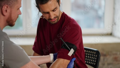 Close-up shooting: A bearded brunette man in a gray T-shirt tightens a tourniquet with another bearded brunette man with long hair in a red T-shirt. Training of practical classes of first aid photo