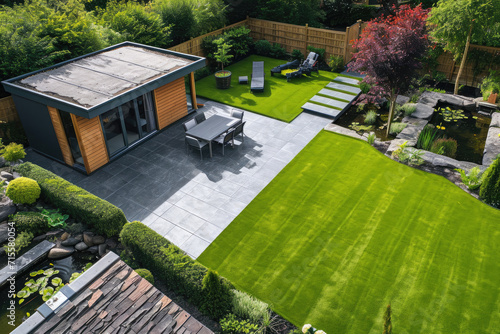 high view of a back garden with artificial grass, grey paving slab patio, summer house garden timber outbuilding, fish pond photo
