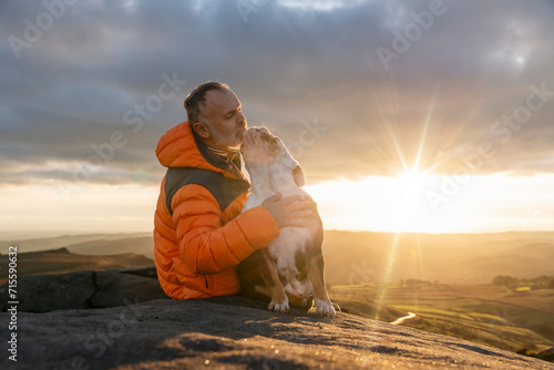 old mature man hiking in mountains with his dog, exercise and fitness for wellness, healthy lifestyle and smile. Face of a senior mature gentleman with bulldog sitting on a rock, enjoying a calm day photo