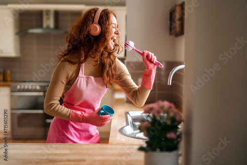 Fotografie Redhead woman washing dishes in the kitchen and listening to music by wireless h