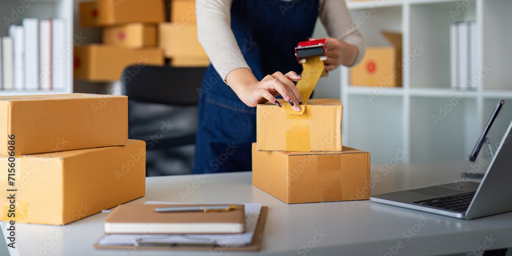 Woman use scotch tape to attach parcel box to prepare goods for the process of packaging, shipping, online sale internet marketing ecommerce concept startup business idea - obrazy, fototapety, plakaty 