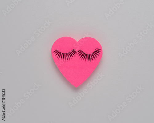 Heart shape pink paper with eyelashes. Valentines or woman's day background design. Minimal flat lay.