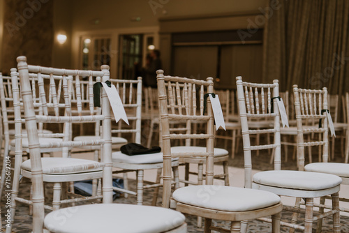Beige, wooden chiavari chairs set out with placenames for a wedding ceremony photo