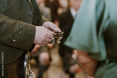 close up of a man holding silver quaich in his hands beside a bridesmaid in green dress at a Scottish wedding