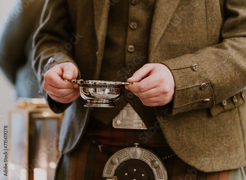 Man in kilt holding scottish quaich with whisky in his hand