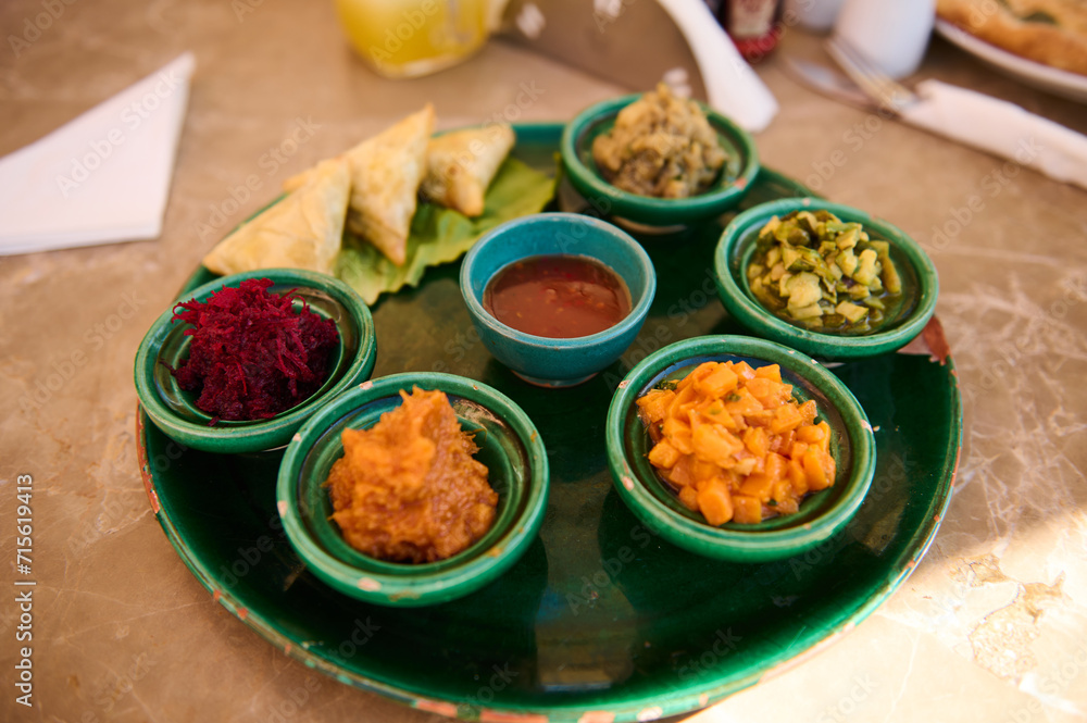 Top view table in restaurant with Moroccan traditional dish, vegetarian salads and sauce served in small ceramic tagines Top view table in restaurant with Moroccan traditional dish, vegetarian salads and sauce served in small ceramic tagines