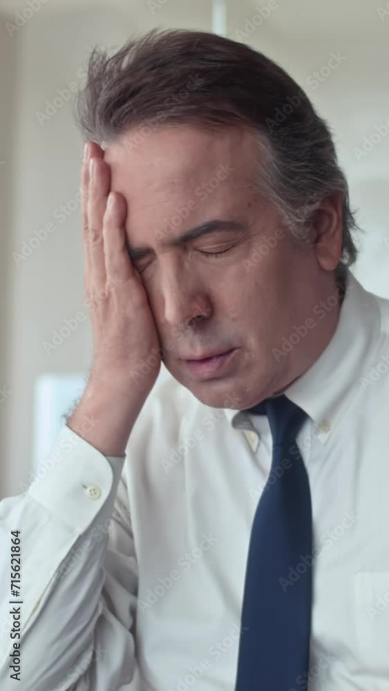Vertical shot of exhausted mature businessman with headache working overtime at office