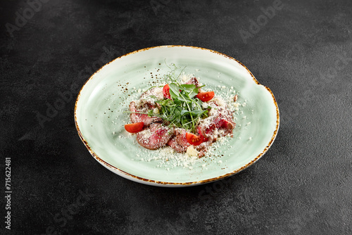 Roast beef carpaccio with Parmesan, arugula, and tomatoes on a speckled turquoise plate