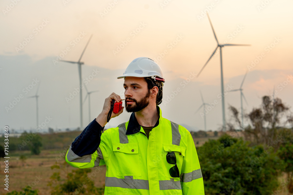 Portrait technician worker man use walkie talkie to contact his co-worker in evening with windmill or wind turbine on the background. Portrait technician worker man use walkie talkie to contact his co-worker in evening with windmill or wind turbine on the background.