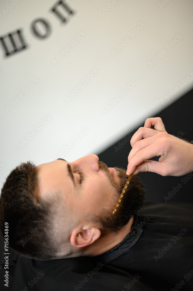 Barber combs beard with comb while shaving Caucasian man Barber combs beard with comb while shaving Caucasian man
