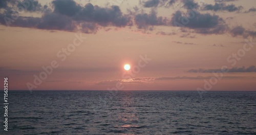 Bright orange sunset colorful sky with pink and velvet with dark clouds and water - sun in center of the frame