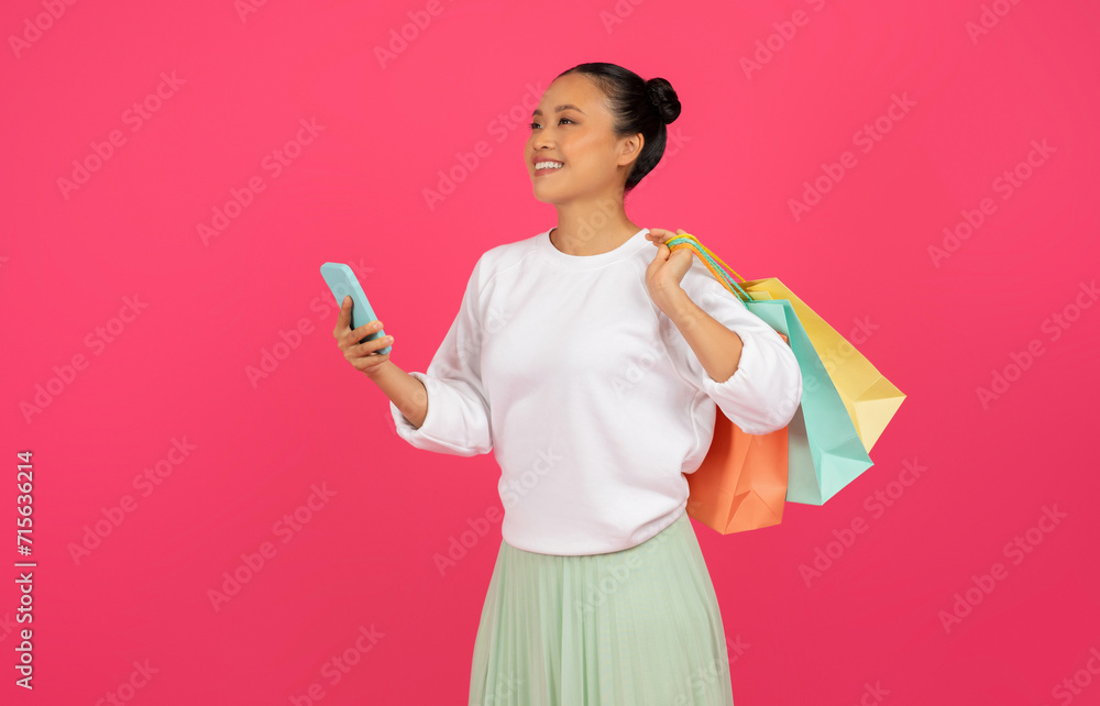 Smiling asian woman holding smartphone and bright shopping bags Smiling asian woman holding smartphone and bright shopping bags