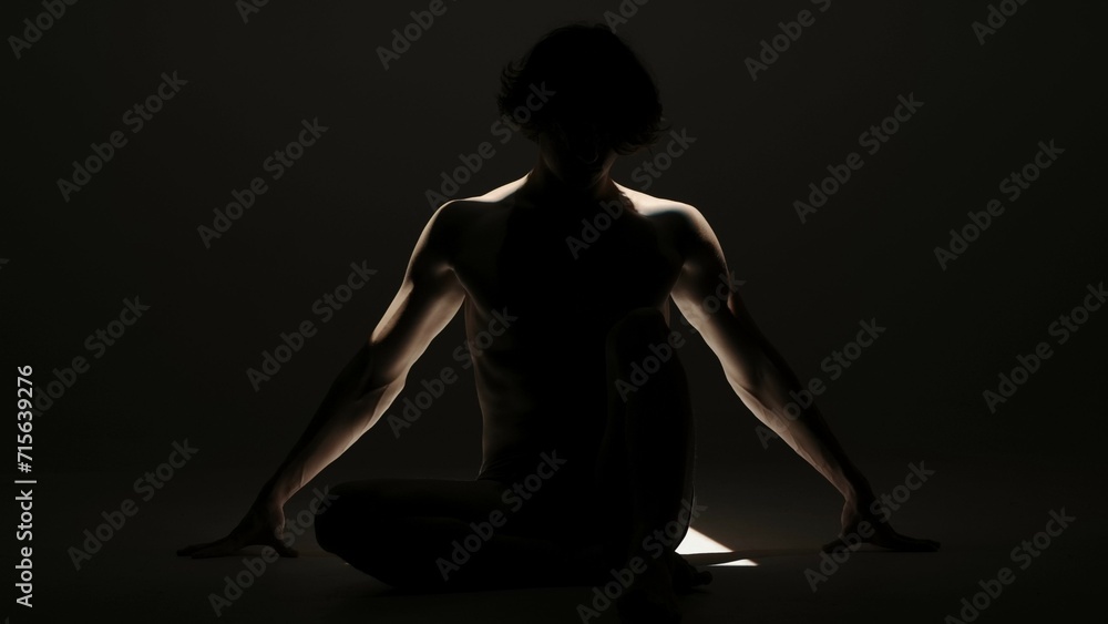 Portrait of male model in studio on the black background under spotlight. Attractive man silhouette posing on the floor at the camera.