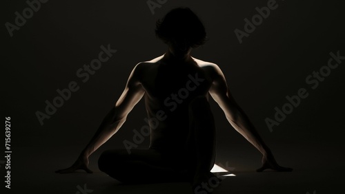Portrait of male model in studio on the black background under spotlight. Attractive man silhouette posing on the floor at the camera.