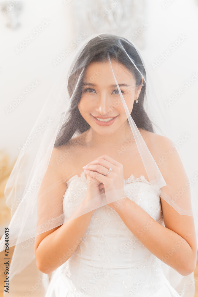 A beautiful, smiling Southeast Asian bride in wedding veil while praying with rings on her finger. Wedding preparation concept. A beautiful, smiling Southeast Asian bride in wedding veil while praying with rings on her finger. Wedding preparation concept.
