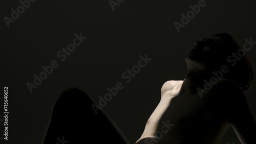 Portrait of male model in studio on the black background under spotlight. Attractive man silhouette posing under ray of light at the camera.