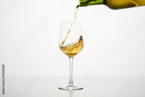 White wine pouring from green bottle, close up shot on white isolated background.