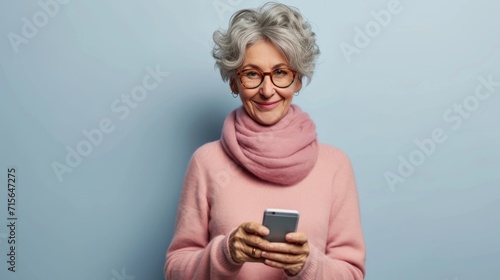 An older woman radiates joy as she holds a mobile smartphone, smiling warmly against an isolated light blue background, embodying modern technology and happiness
