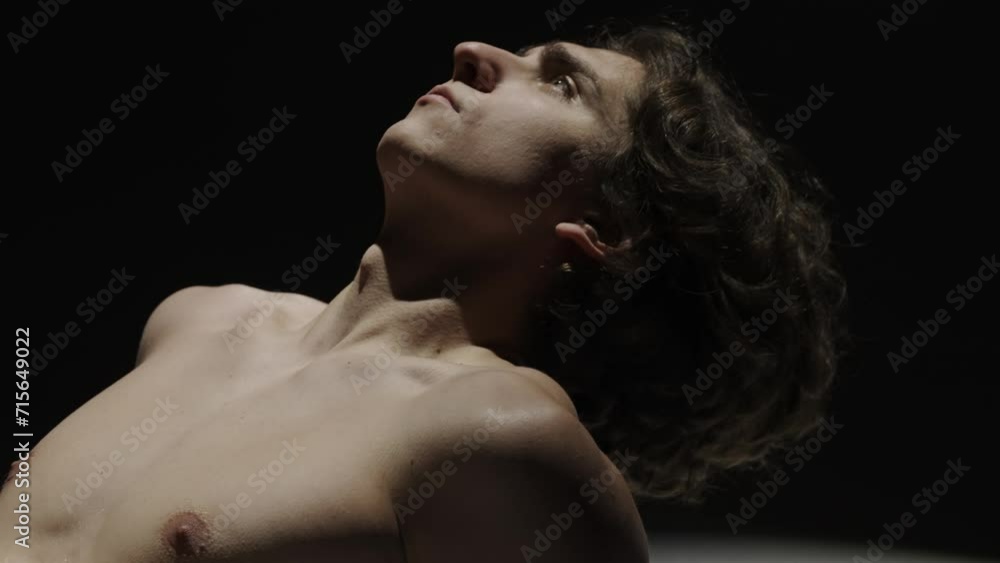 Portrait of male model on the black background in spotlight. Handsome man silhouette posing on the floor at the camera. Slow motion. Portrait of male model on the black background in spotlight. Handsome man silhouette posing on the floor at the camera. Slow motion.