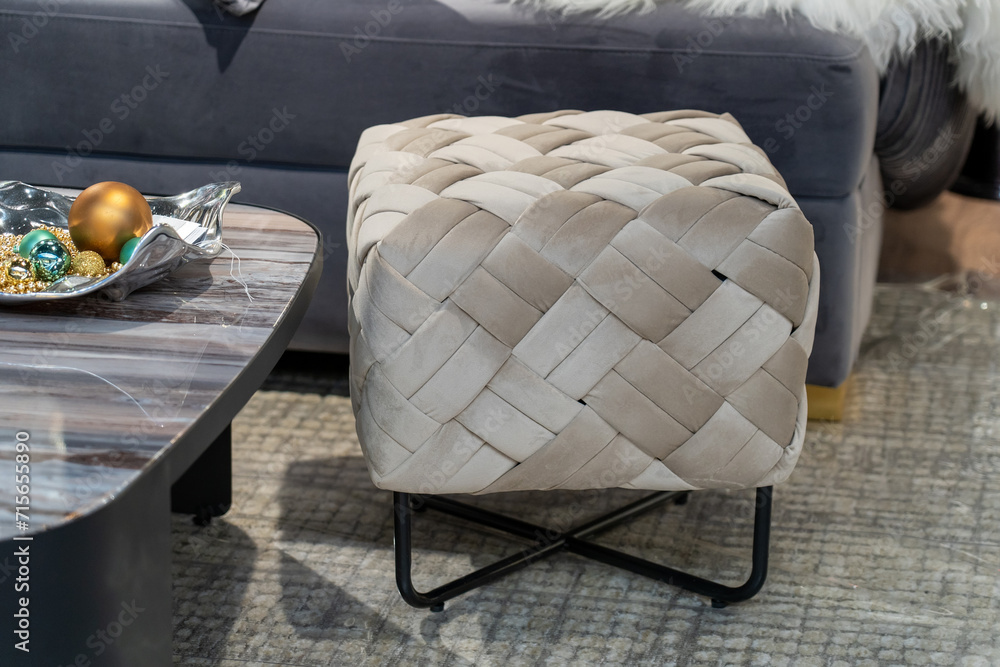 Grey stool with woven pattern stands in front of grey couch. Grey stool with woven pattern stands in front of grey couch.